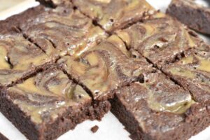 Nine square pieces of Keto Caramel Brownies with a glossy, swirled caramel topping, arranged on parchment paper.