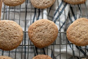 Low Carb Gluten Free Oatmeal Spice Cookies cooling on a metal rack over a plaid cloth. The cookies are golden brown and appear freshly baked, with a textured surface.