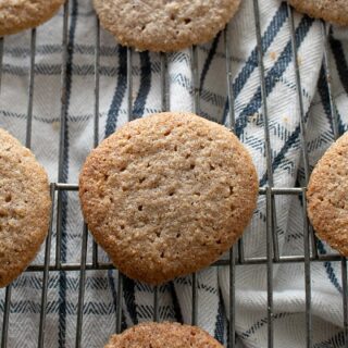 Low Carb Gluten Free Oatmeal Spice Cookies cooling on a metal rack over a plaid cloth. The cookies are golden brown and appear freshly baked, with a textured surface.