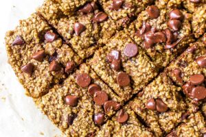 Close-up of square-shaped Gluten Free Chocolate Chip Oat Bars with Pumpkin topped with melted chocolate chips. The bars have a crumbly texture with oats visibly mixed in. The image captures a warm, freshly baked appearance.