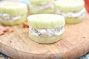 Keto Bacon Herbed Cream Cheese Cucumber Bites, with a cream cheese filling on a wooden cutting board, offering a refreshing and crunchy snack option.