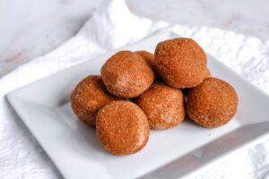 A square white plate holds a pyramid stack of round, Keto Pumpkin Pie Spice Fat Bombs. The background is white, giving a clean and minimalistic look.
