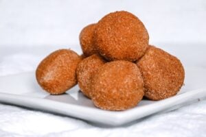 A square white plate holds a pyramid stack of round, Keto Pumpkin Pie Spice Fat Bombs. The background is white, giving a clean and minimalistic look.