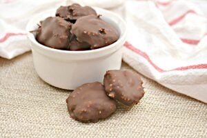 A bowl of homemade Copycat Keto Almond Joy Bites with a crunchy texture, displayed on a natural canvas surface with a hint of a red-and-white napkin peeking in the background.