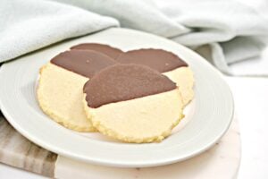 A plate with four Keto Shortbread Cookies, each half-dipped in chocolate, on a light green plate. A light blue cloth is partially visible in the background.