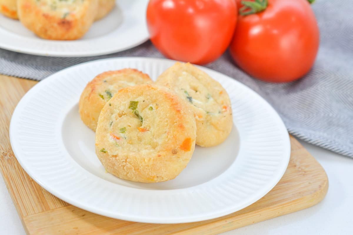 Keto Cream Cheese Rolls with Tomato and Basil on a white plate, with fresh tomatoes in the background on a wooden cutting board.
