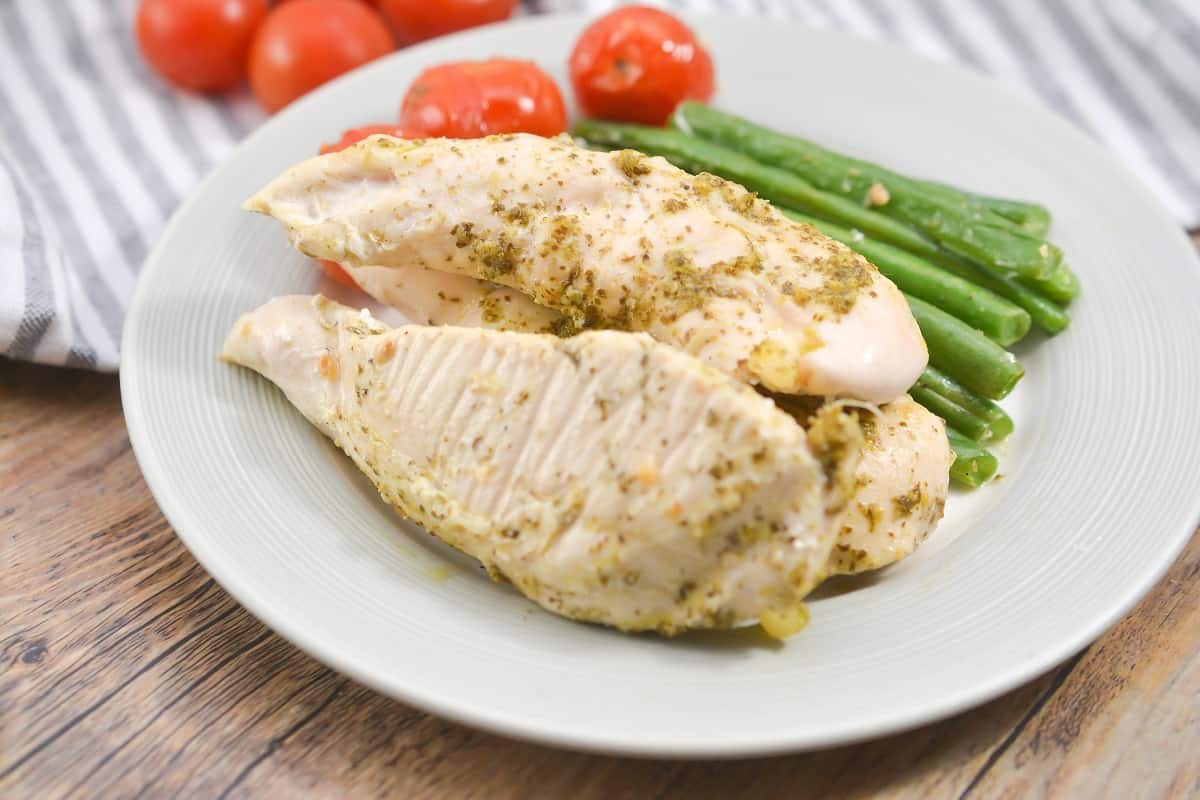 Keto Pesto Chicken with green beans and cherry tomatoes on a white plate, that is sitting on a wooden background. With cherry tomatoes toward the top of the plate.