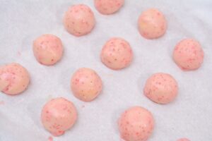 Twelve pink, speckled Strawberry Shakeology Donut Holes are arranged on a parchment-lined baking sheet.