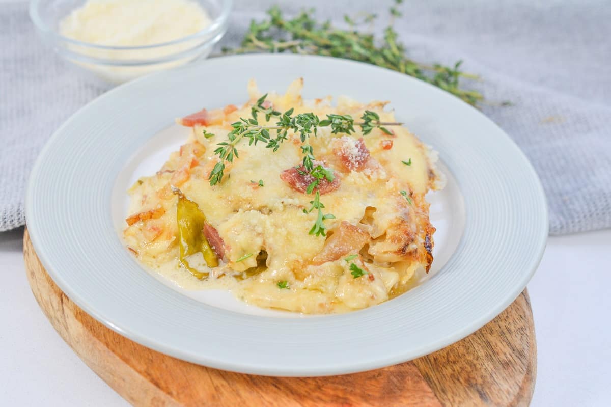 A serving of creamy Keto Cabbage Au Gratin topped with golden melted cheese, and a sprig of fresh thyme, presented on a white plate.