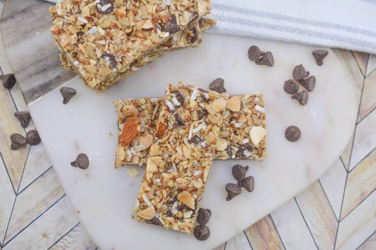 Homemade Keto Granola Bars with almonds and chocolate chips on a white stone cutting board. Which is situated on a dimensional looking background.