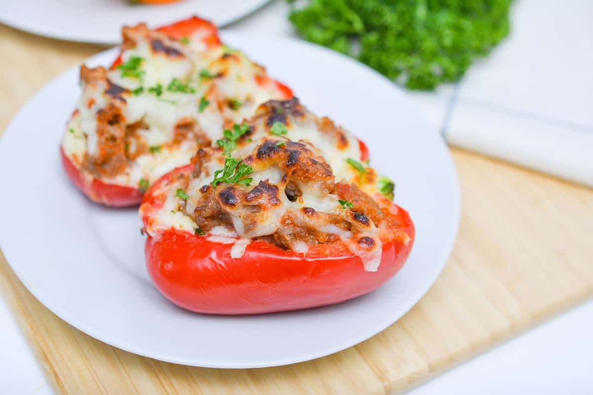 Keto Stuffed Peppers filled with a mix of ground Italian sausage, vegetables, and topped with melted cheese, garnished with parsley on a white plate.