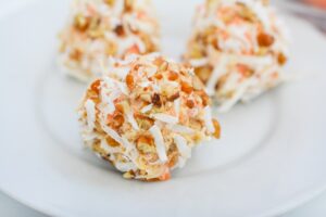 Closeup of Keto Carrot Cake Balls on a white plate, clearly showing the texture of coconut, and small bits of bright orange carrots.