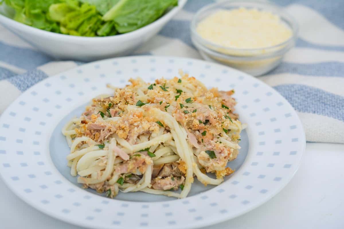 A plate of creamy Keto Tuna Noodle Casserole topped with pork rind crumbs and parsley, served on a white plate with a dotted pattern.
