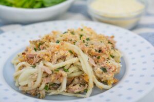 A plate of creamy Keto Tuna Noodle Casserole topped with pork rind crumbs and parsley, served on a white plate with a dotted pattern.