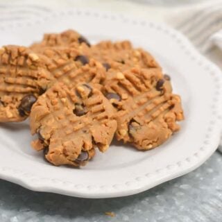 A plate of homemade peanut butter cookies with chocolate chips on a white plate, placed on a light blue textured surface with a striped napkin nearby.