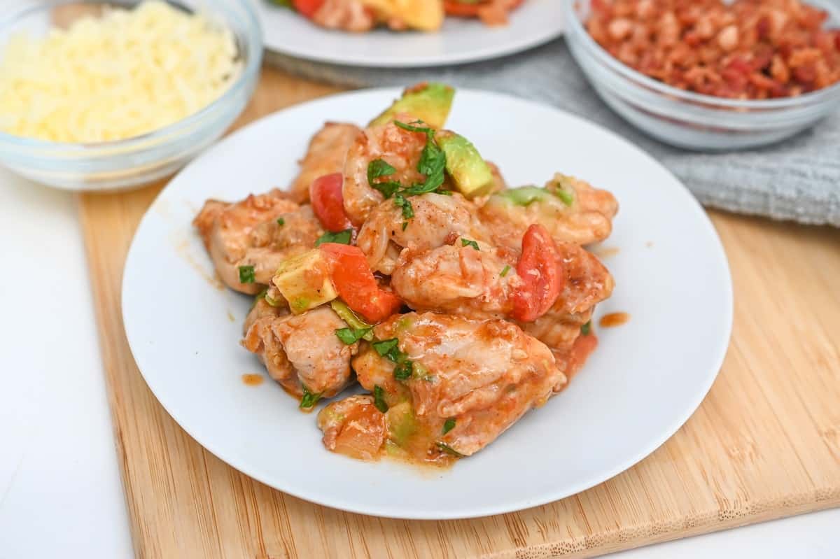 A plate of Keto Monterey Chicken garnished with avocado, tomato, and herbs.