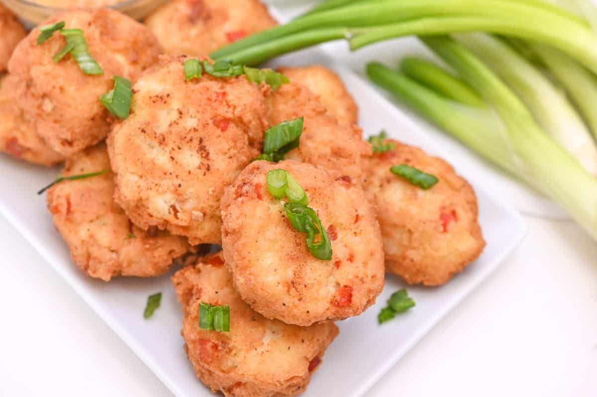 A plate of crispy fried Keto Chicken Fritter, garnished with sliced green onions, sitting on a rectangular white plate.