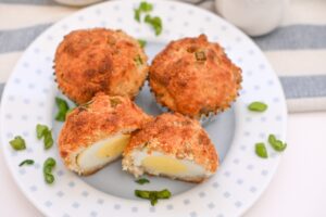 A plate of homemade Keto Egg Muffins With Sausage and Cheese with one cut in half to reveal the cooked egg inside, garnished with fresh herbs. Sitting on a white plate with a repeating small blue square pattern along the edge.