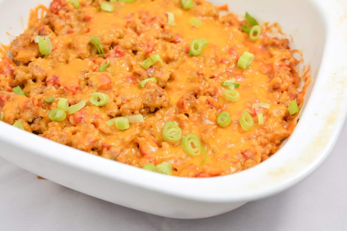 A close-up view of Easy Keto Taco Casserole topped with melted cheddar cheese and garnished with sliced green onions, ready to be served. 