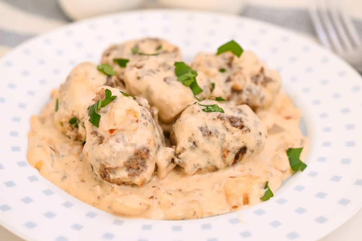 Keto Swedish Meatballs garnished with chopped parsley, on a white plate brimmed with tiny blue squares.