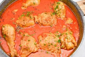 A large skillet filled with Keto Chicken Paprikash covered in a rich red tomato sauce, garnished with chopped parsley. The vibrant sauce gives the dish a hearty and appetizing appearance.