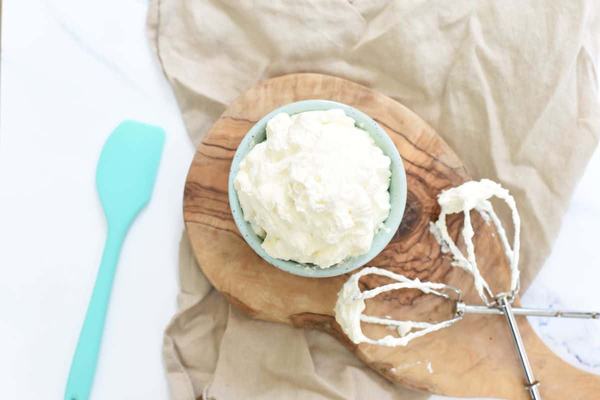 Homemade whipped cream in a teal bowl with a spatula.