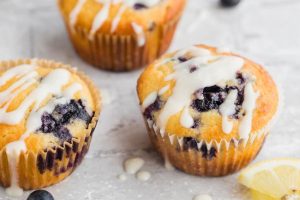 Lemon Blueberry Muffins drizzled with icing on a white surface.