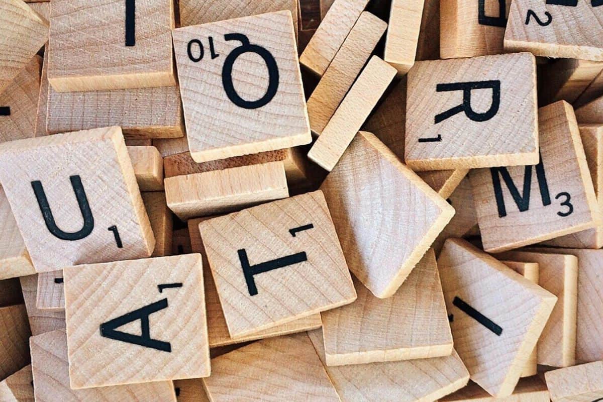 A pile of wooden Scrabble tiles displays black letters and numbers, with several scattered and partially covering each other like a delightful puzzle. Among the visible letters—T, R, A, O, M, U—you might even discover some clever keto Hallowen hacks spelled out!