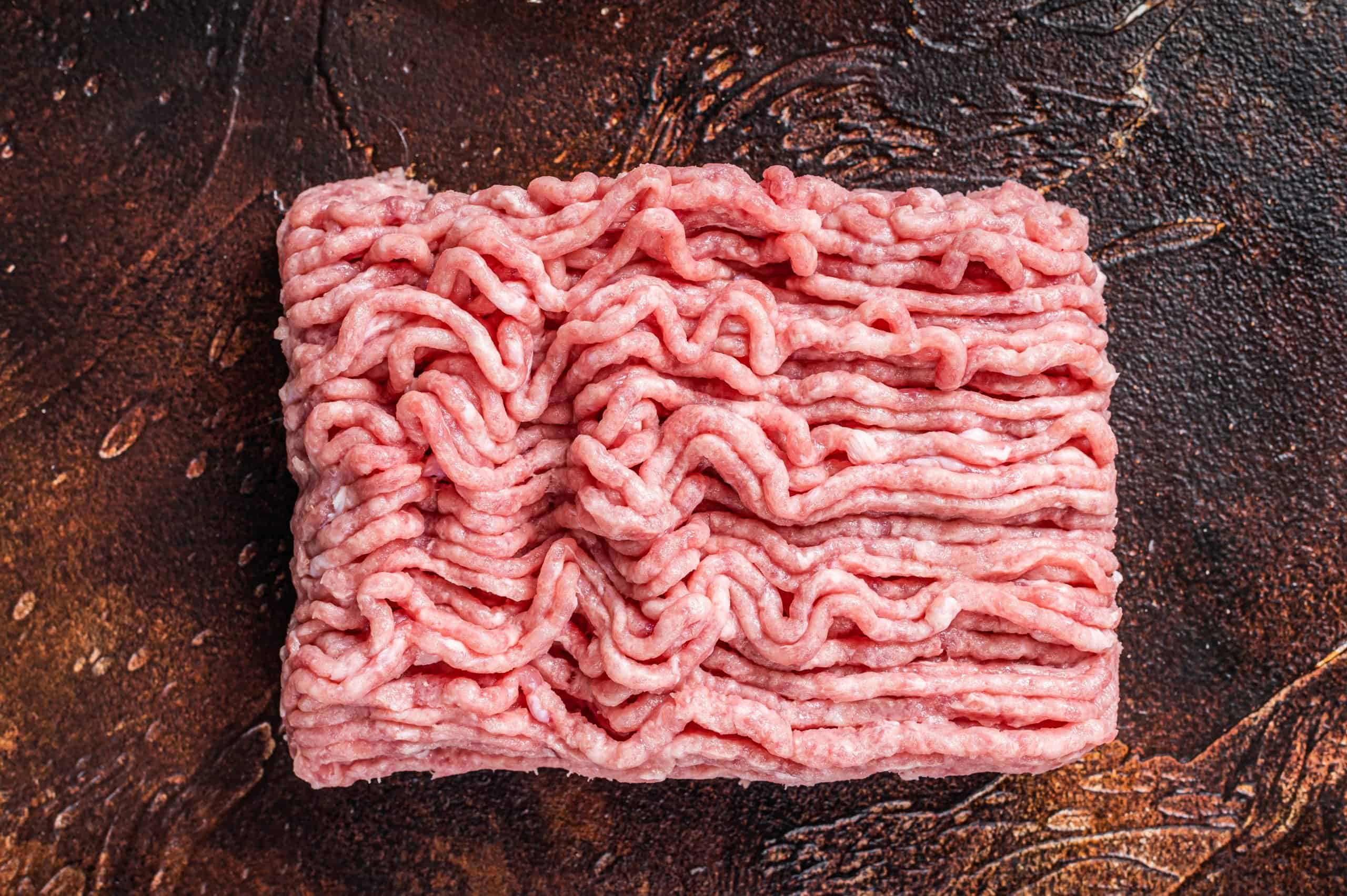 Raw ground chicken or turkey meat on brown table. Dark background. Top View.