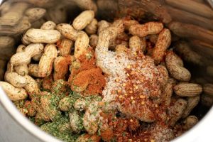 A pot filled with unpeeled peanuts topped with a mixture of spices, including red chili flakes, salt, paprika, and dried herbs, creates the perfect no added sugar snack for seasoning or cooking.