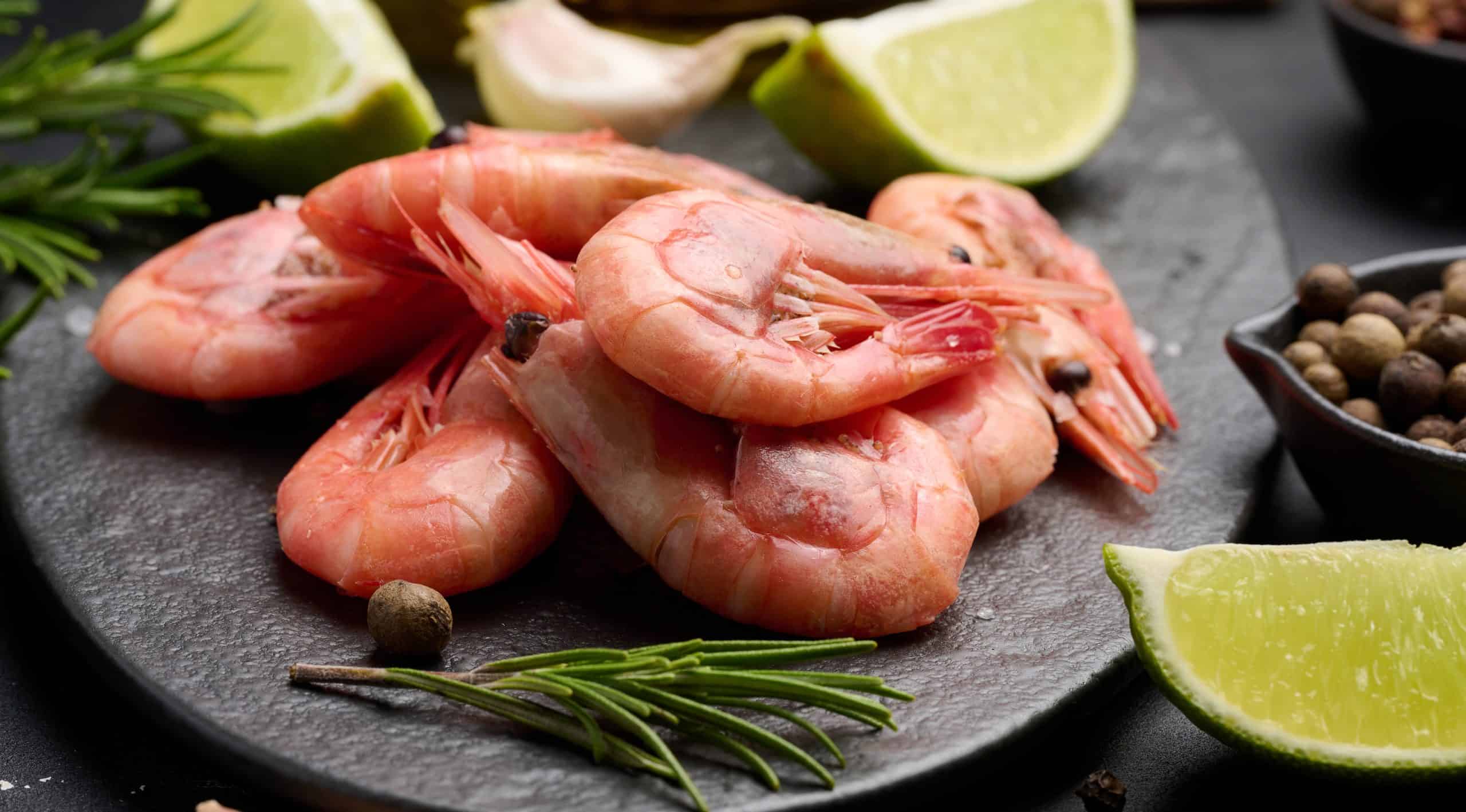 Boiled shrimp on a board, lemon slices, spices on a black background