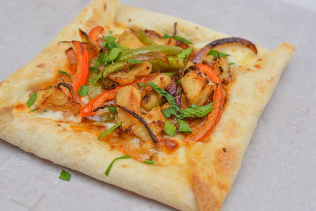 A square pizza topped with grilled chicken, green and red bell peppers, onions, and fresh herbs on a light, crispy crust.