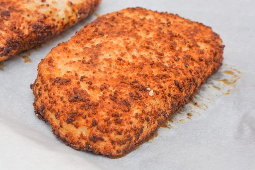 Close-up of a golden-brown, crispy breaded food item on parchment paper. The surface is covered in an even, crunchy coating, suggesting it might be baked or fried.