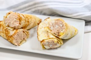 Three crepes filled with a creamy mixture are neatly displayed on a white rectangular plate. A striped kitchen towel is partially visible in the background.