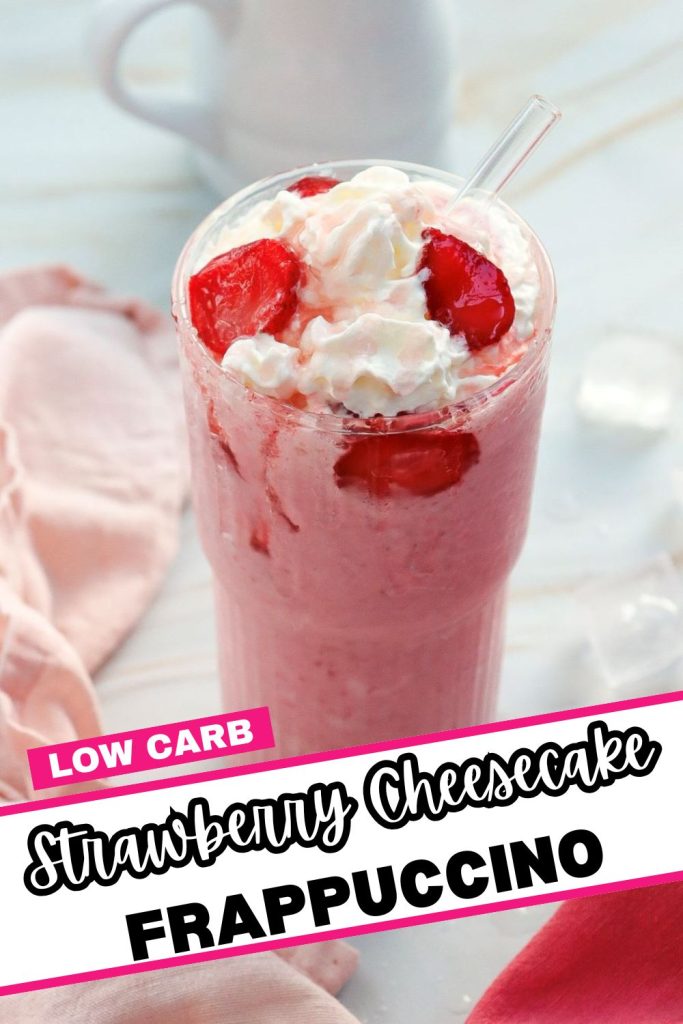 A tall glass of strawberry cheesecake frappuccino topped with whipped cream and strawberry slices. A straw is inserted. A pink napkin and ice cubes are in the background. The text reads "Low Carb Strawberry Cheesecake Frappuccino.