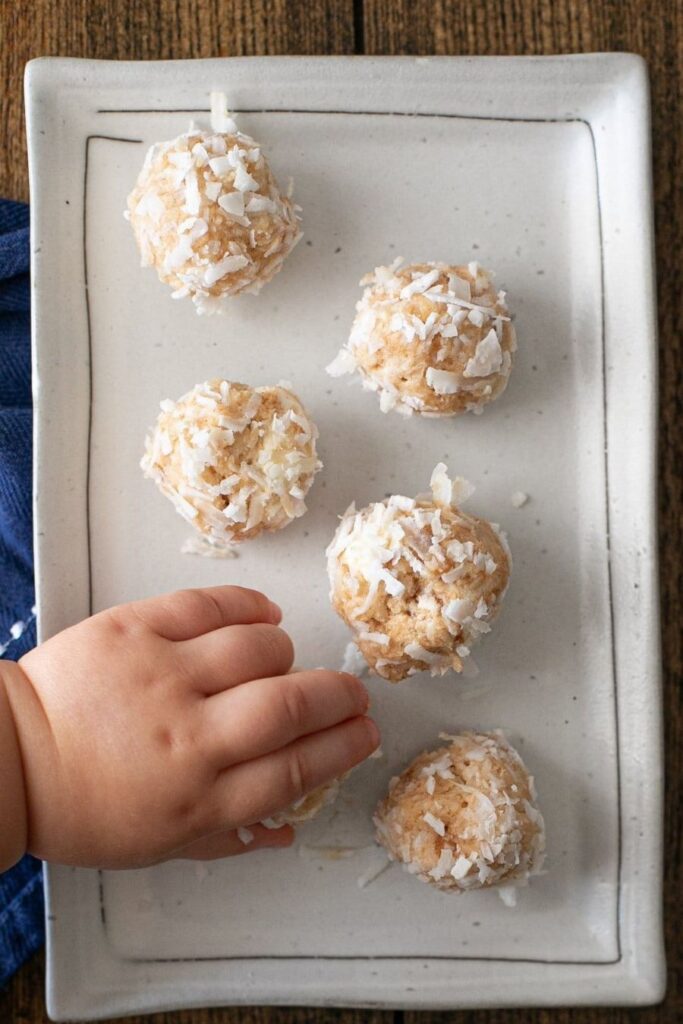 No Bake Peanut Butter Balls on a plate with a child's hand reaching for one.