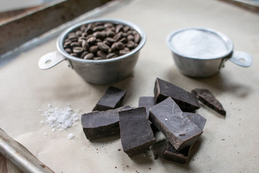 Rich dark chocolate and coffee beans on baking tray, with salt and cocoa powder; perfect for artisanal chocolate making.
