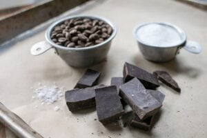 Rich dark chocolate and coffee beans on baking tray, with salt and cocoa powder; perfect for artisanal chocolate making.