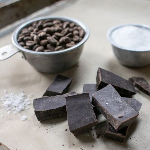 Rich dark chocolate and coffee beans on baking tray, with salt and cocoa powder; perfect for artisanal chocolate making.